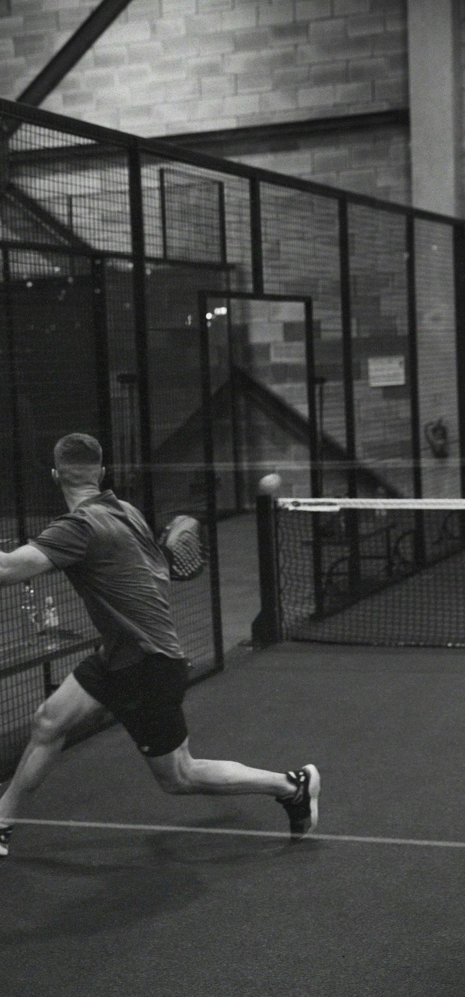 Padel player lunging for a low ball on an indoor court